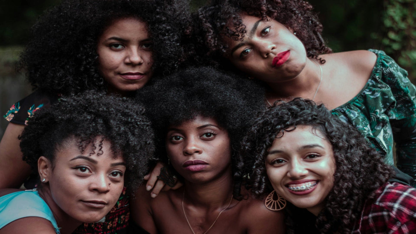 Five women with natural hairstyles posing together outdoors.